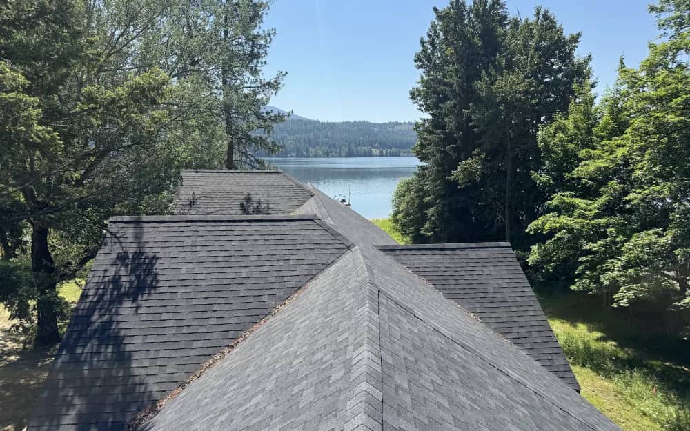 Elevated view of a gray asphalt shingle roof with Cocolalla Lake and forest in the distance